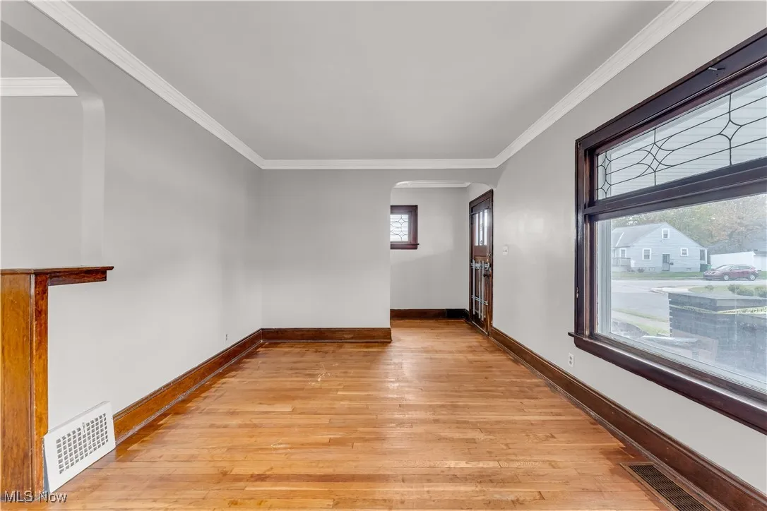 Unfurnished room featuring arched walkways, light wood finished floors, and ornamental molding