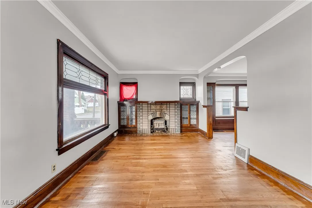 Unfurnished living room with ornamental molding, light wood finished floors, healthy amount of natural light, arched walkways, and a brick fireplace