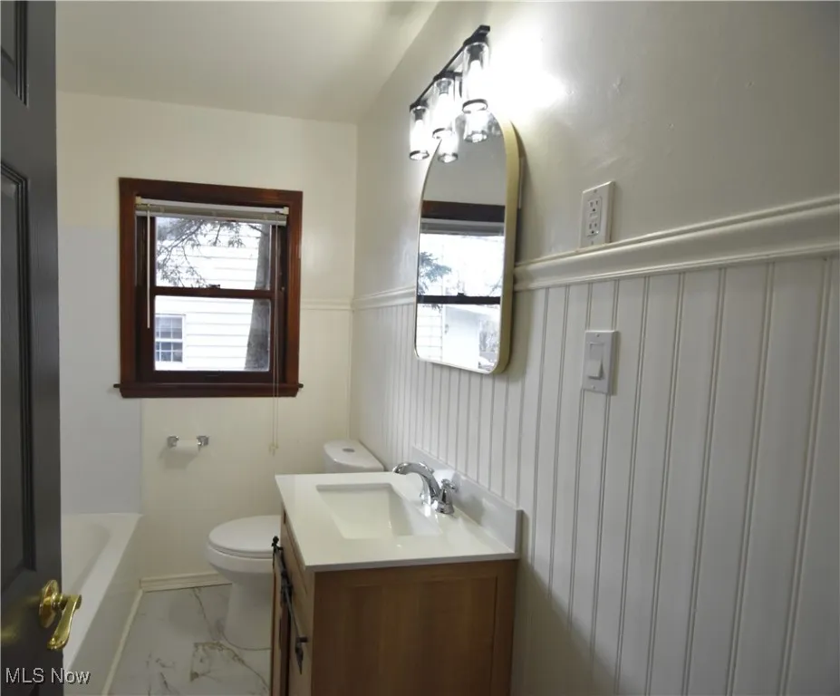 Bathroom with wainscoting, vanity, plenty of natural light, and light marble finish floors