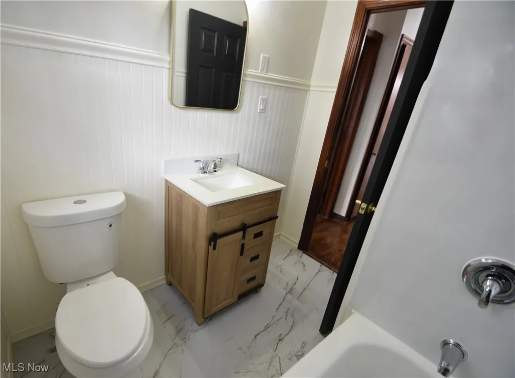 Full bathroom featuring light marble finish floors, a wainscoted wall, a bathtub, and vanity