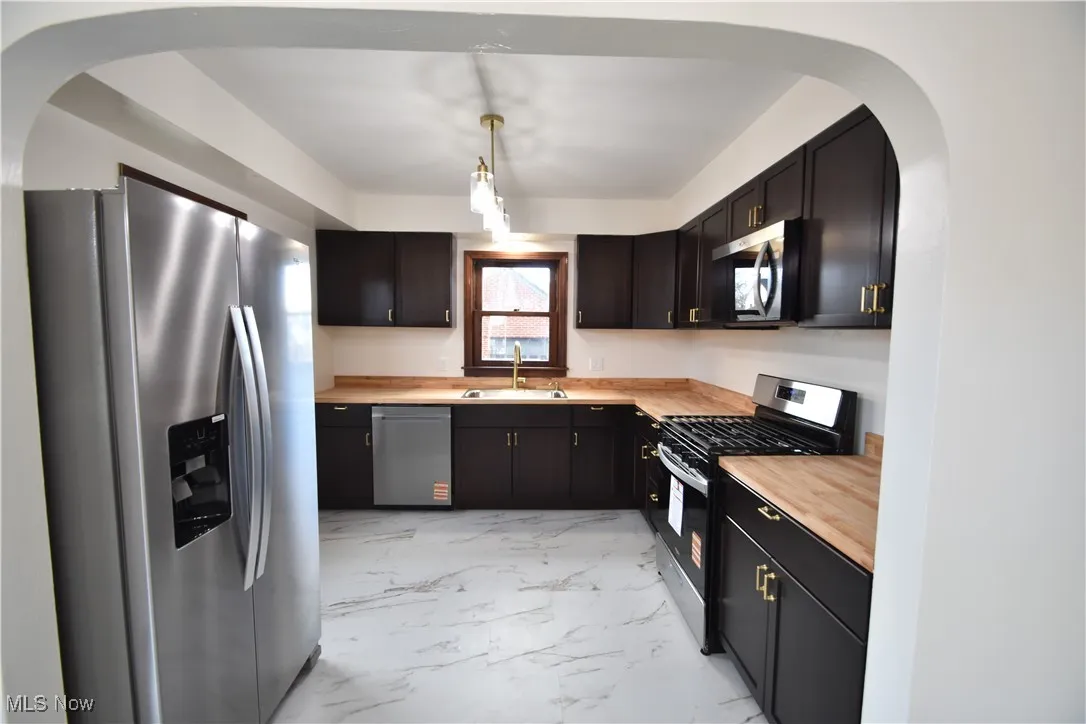 Kitchen featuring stainless steel appliances, arched walkways, light marble finish floors, wood counters, and decorative light fixtures
