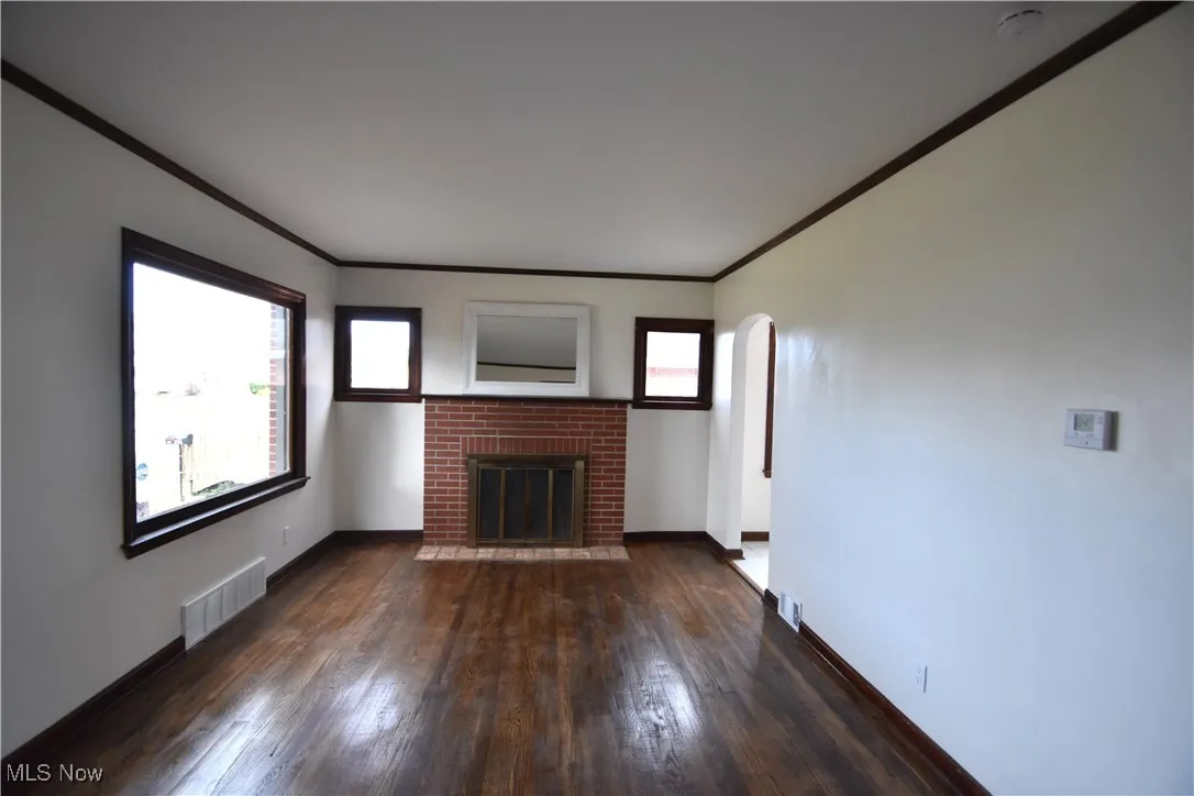 Unfurnished living room featuring ornamental molding, arched walkways, a fireplace, dark wood finished floors, and plenty of natural light