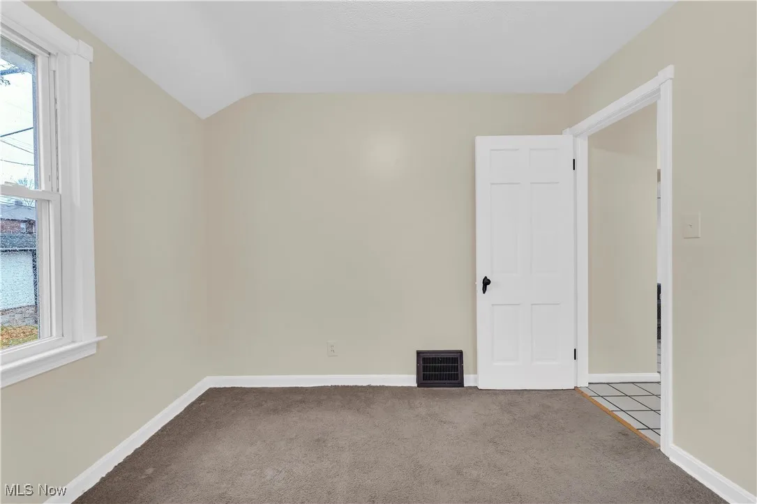 Empty room featuring carpet and lofted ceiling