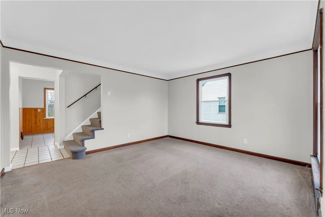 Carpeted empty room featuring ornamental molding and stairs