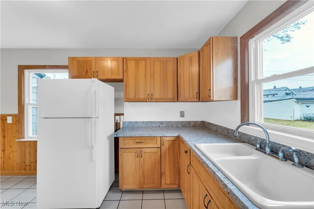 Kitchen with freestanding refrigerator, light tile patterned flooring, wood walls, light countertops, and wainscoting