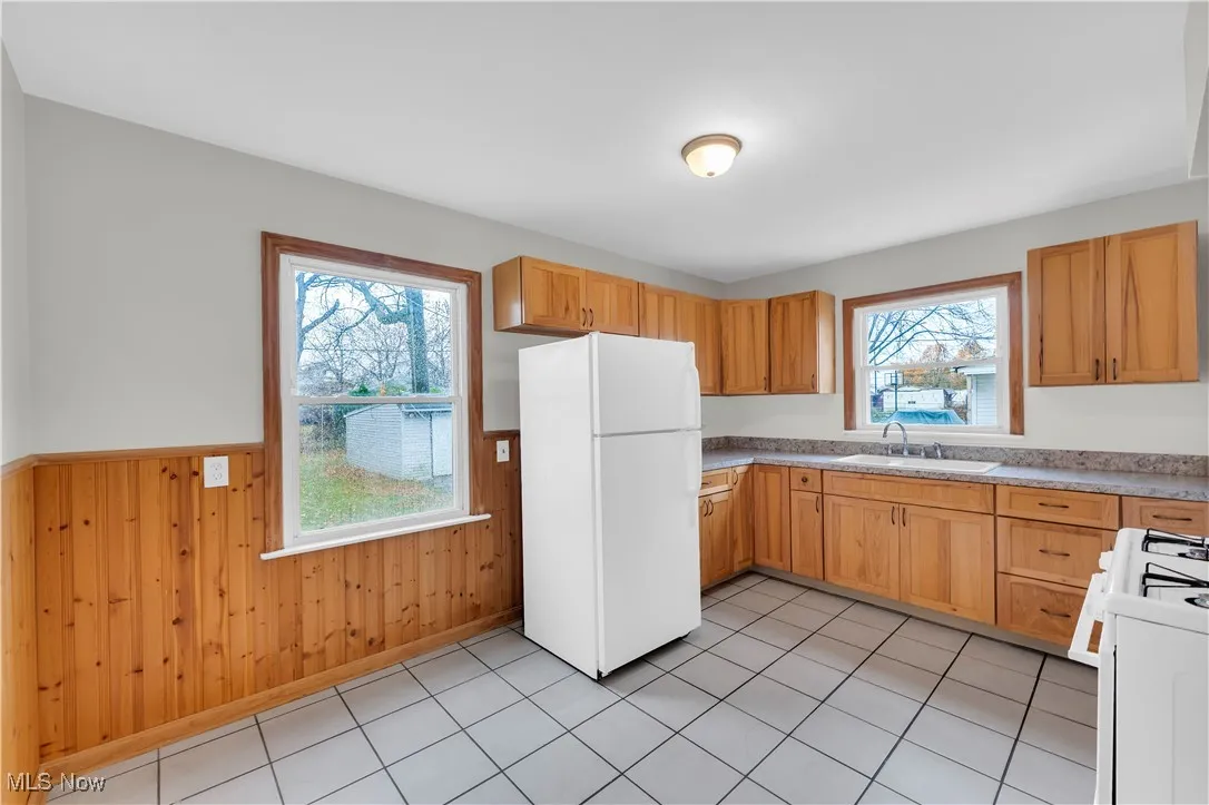 Kitchen with white appliances, light countertops, a wainscoted wall, wood walls, and light tile patterned flooring