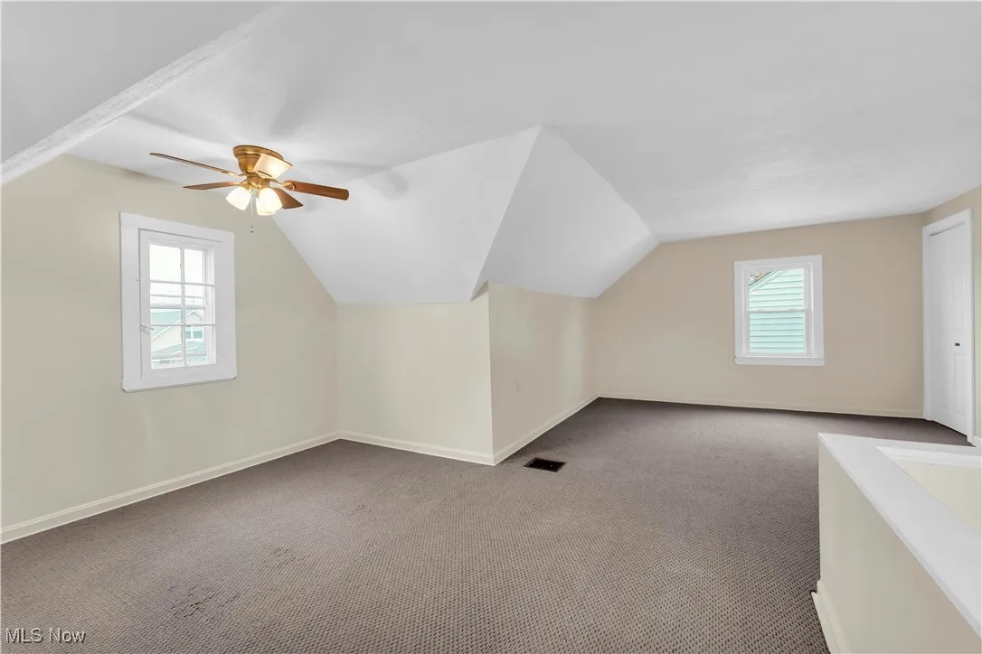 Additional living space featuring vaulted ceiling, carpet, healthy amount of natural light, and a ceiling fan
