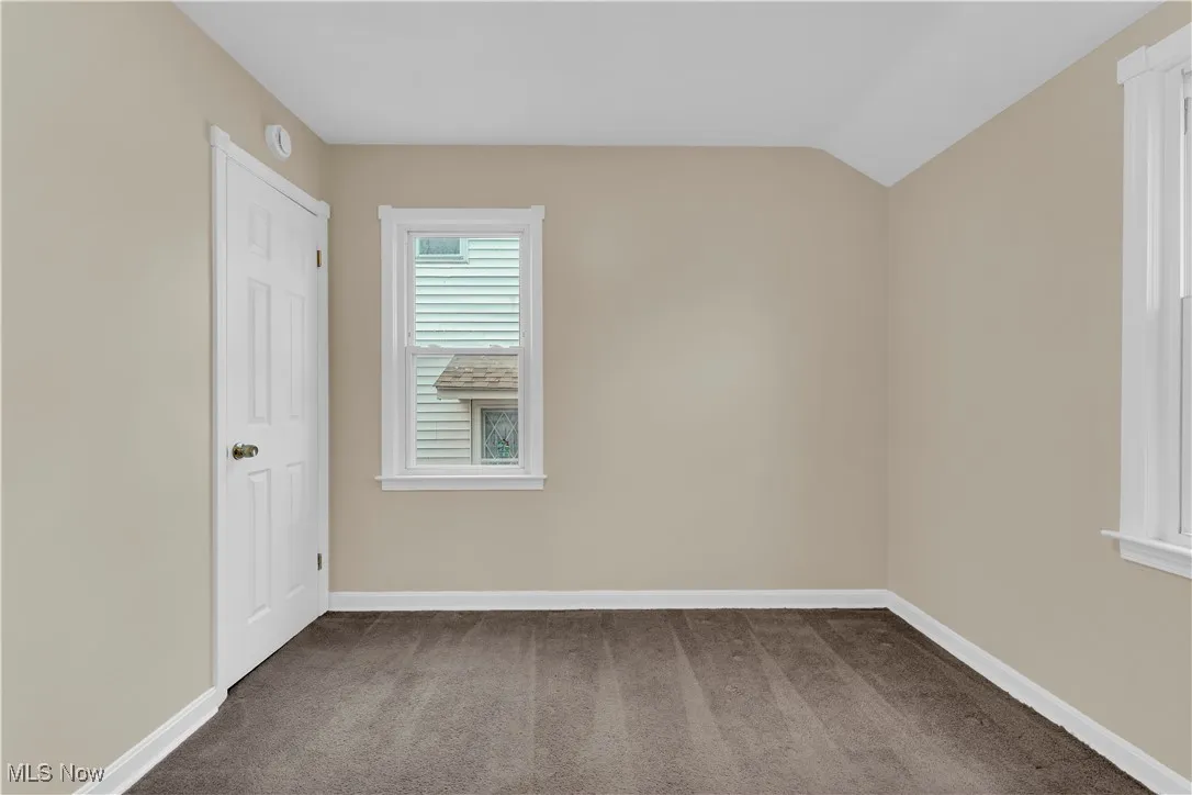 Empty room featuring dark carpet and lofted ceiling