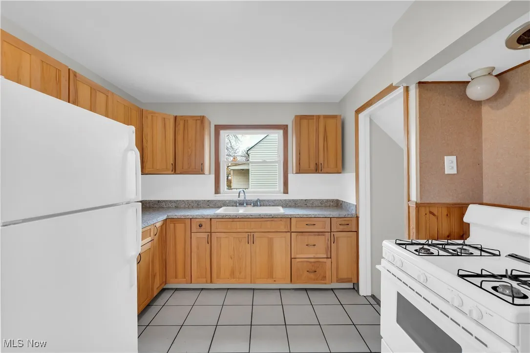 Kitchen featuring white appliances, wainscoting, light countertops, and light tile patterned floors