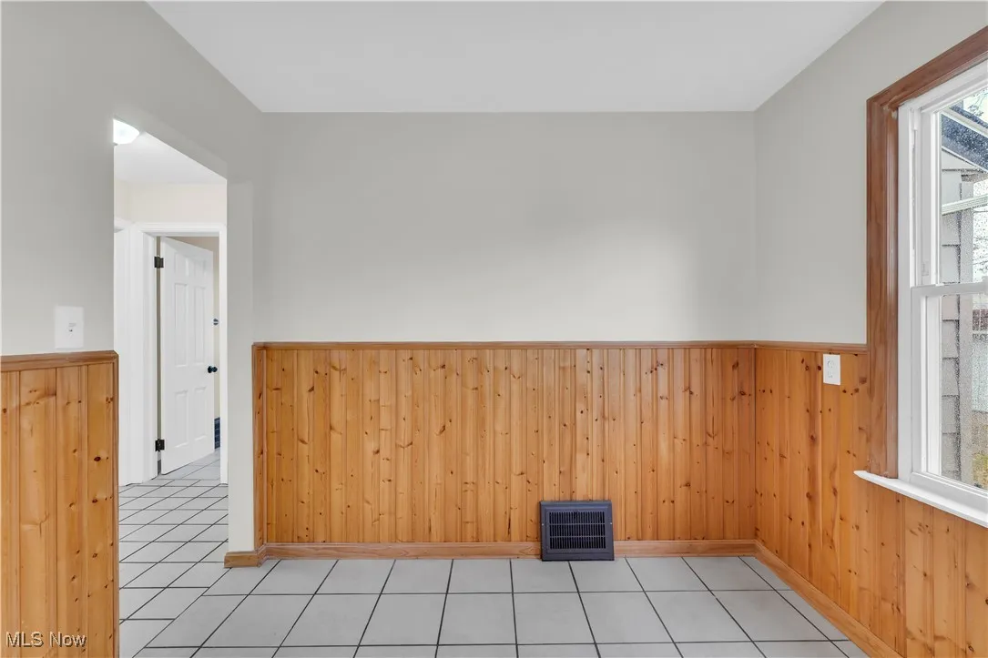 Tiled empty room featuring wood walls, healthy amount of natural light, and wainscoting
