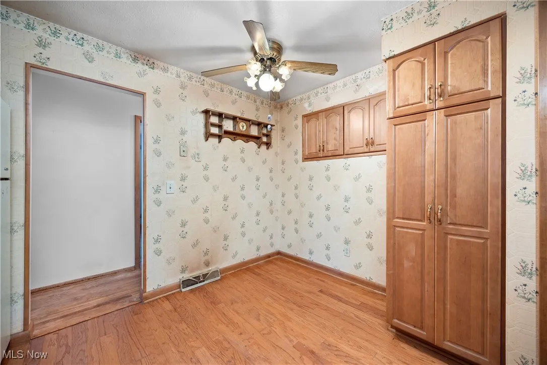 Empty room featuring light wood-type flooring, wallpapered walls, and a ceiling fan