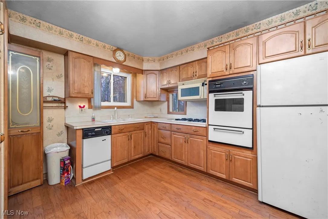 Kitchen featuring white appliances, light countertops, wallpapered walls, a warming drawer, and light wood-style flooring