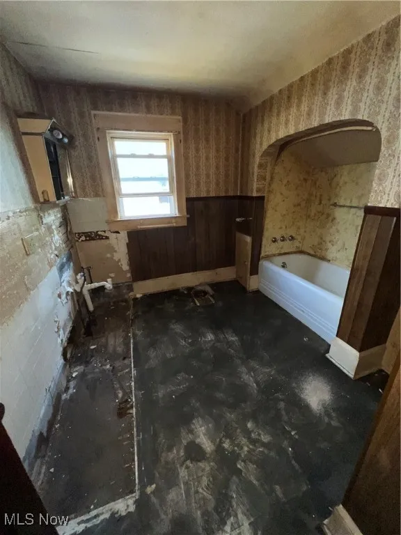 Full bath with wallpapered walls, a bathtub, and a wainscoted wall