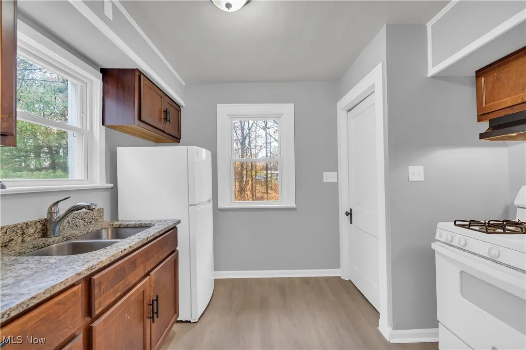 Kitchen with white appliances, light stone countertops, light wood-style floors, brown cabinetry, and under cabinet range hood