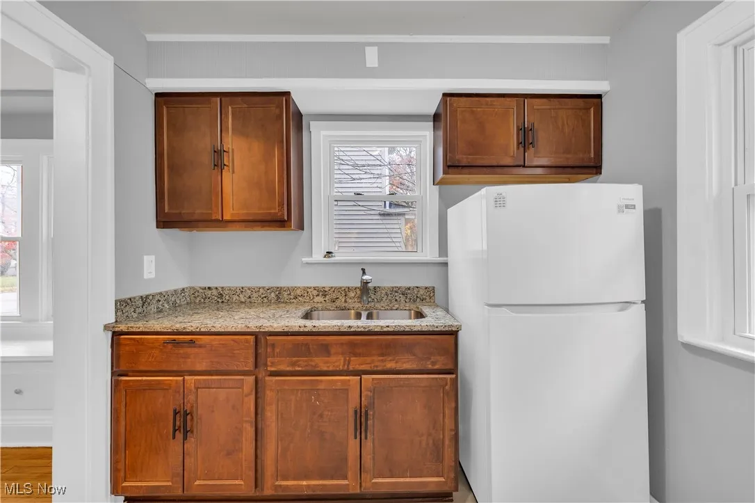 Kitchen featuring freestanding refrigerator, light stone countertops, and brown cabinetry