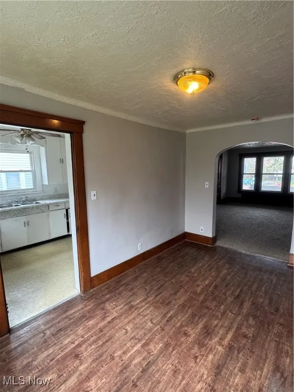Empty room featuring arched walkways, a textured ceiling, dark wood finished floors, ornamental molding, and a ceiling fan