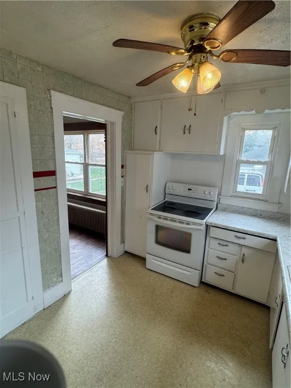 Kitchen with light flooring, white cabinets, range, light countertops, and a textured ceiling