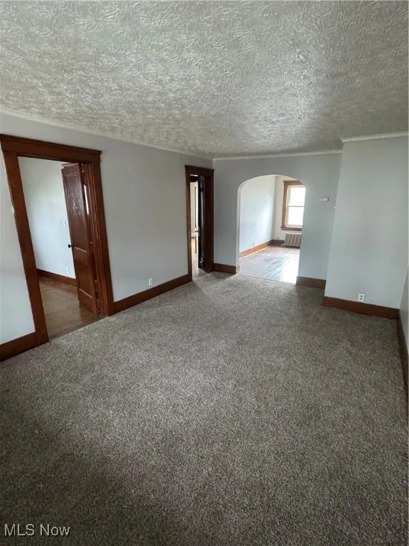 Spare room with arched walkways, carpet floors, radiator heating unit, and a textured ceiling