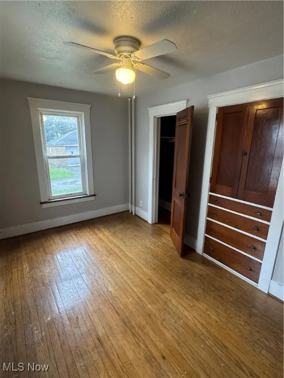 Unfurnished bedroom featuring a textured ceiling, a ceiling fan, light wood finished floors, and a closet
