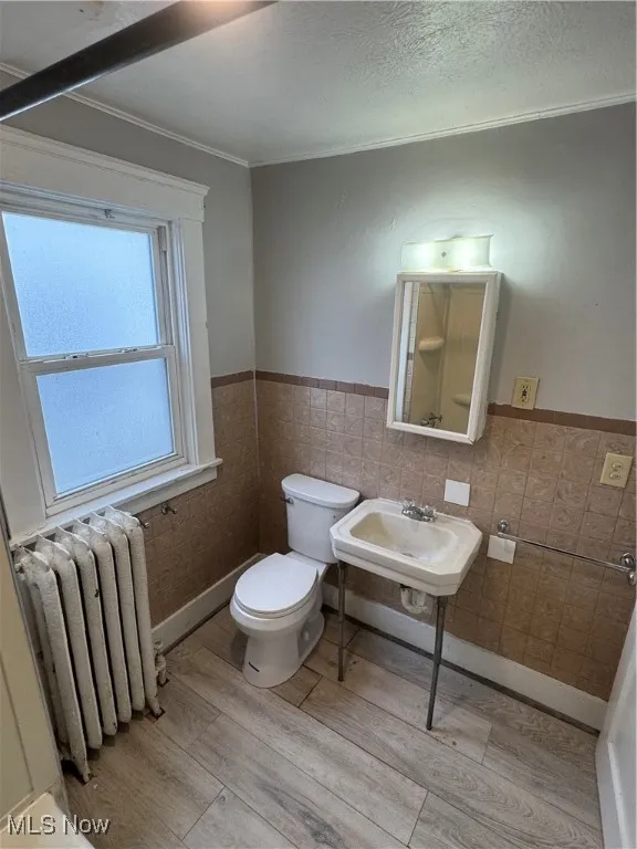 Bathroom featuring radiator heating unit, wainscoting, a textured ceiling, tile walls, and light wood-style floors