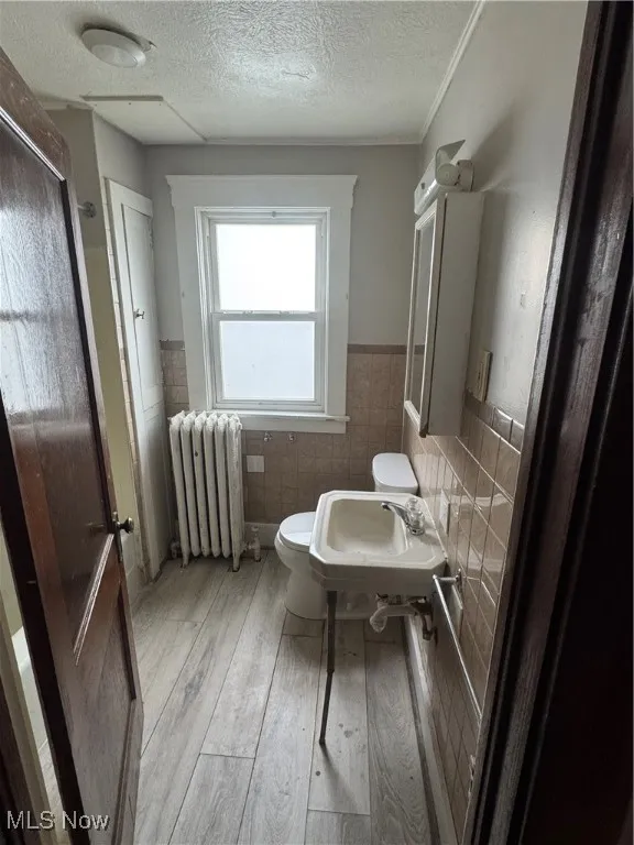 Full bath featuring a wainscoted wall, tile walls, radiator, a textured ceiling, and light wood-type flooring