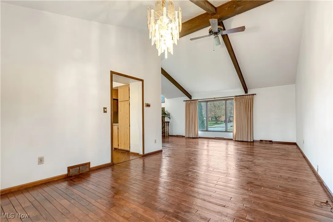 Unfurnished living room featuring beamed ceiling, a chandelier, high vaulted ceiling, wood-type flooring, and ceiling fan