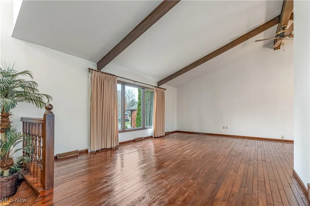 Unfurnished living room with beam ceiling, high vaulted ceiling, hardwood / wood-style flooring, and ceiling fan