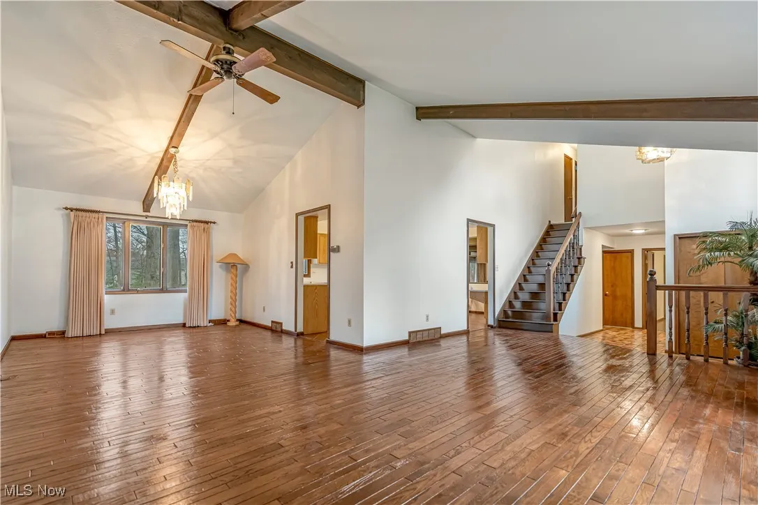 Unfurnished living room featuring a chandelier, high vaulted ceiling, beam ceiling, hardwood / wood-style floors, and stairs