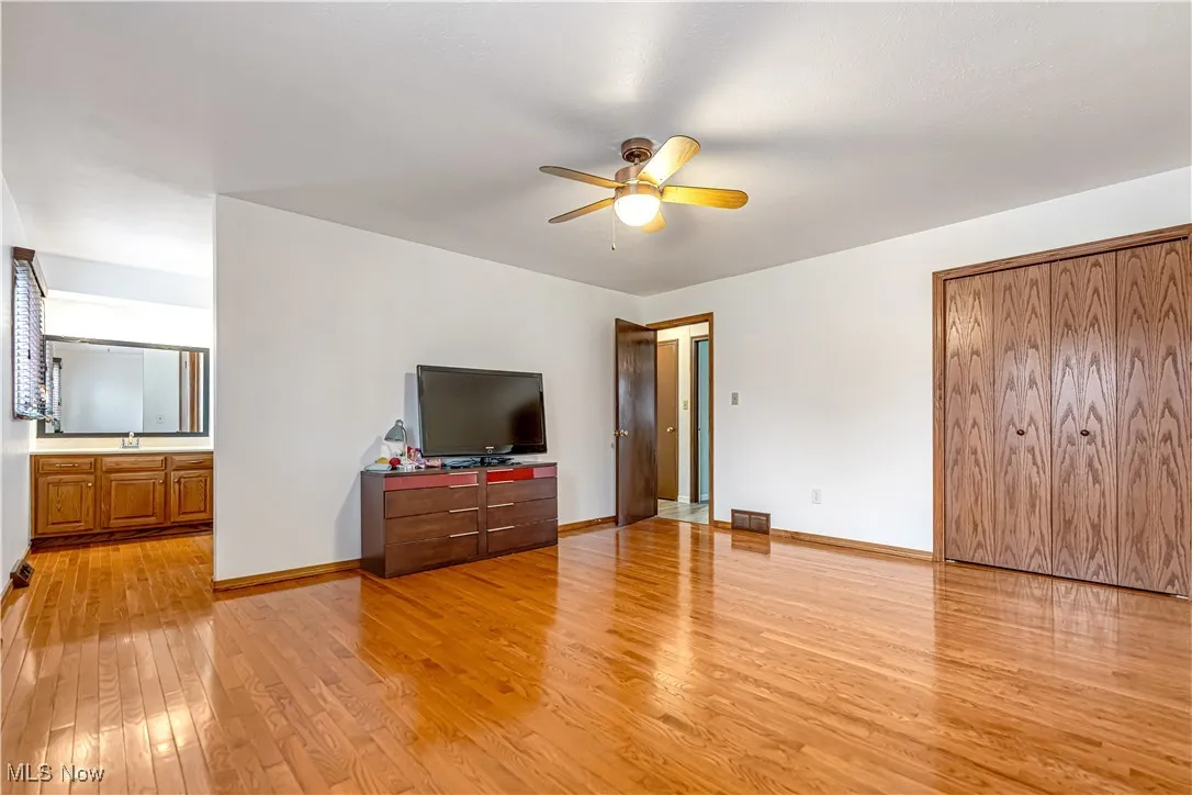 Unfurnished bedroom with light wood-type flooring, ceiling fan, and ensuite bathroom