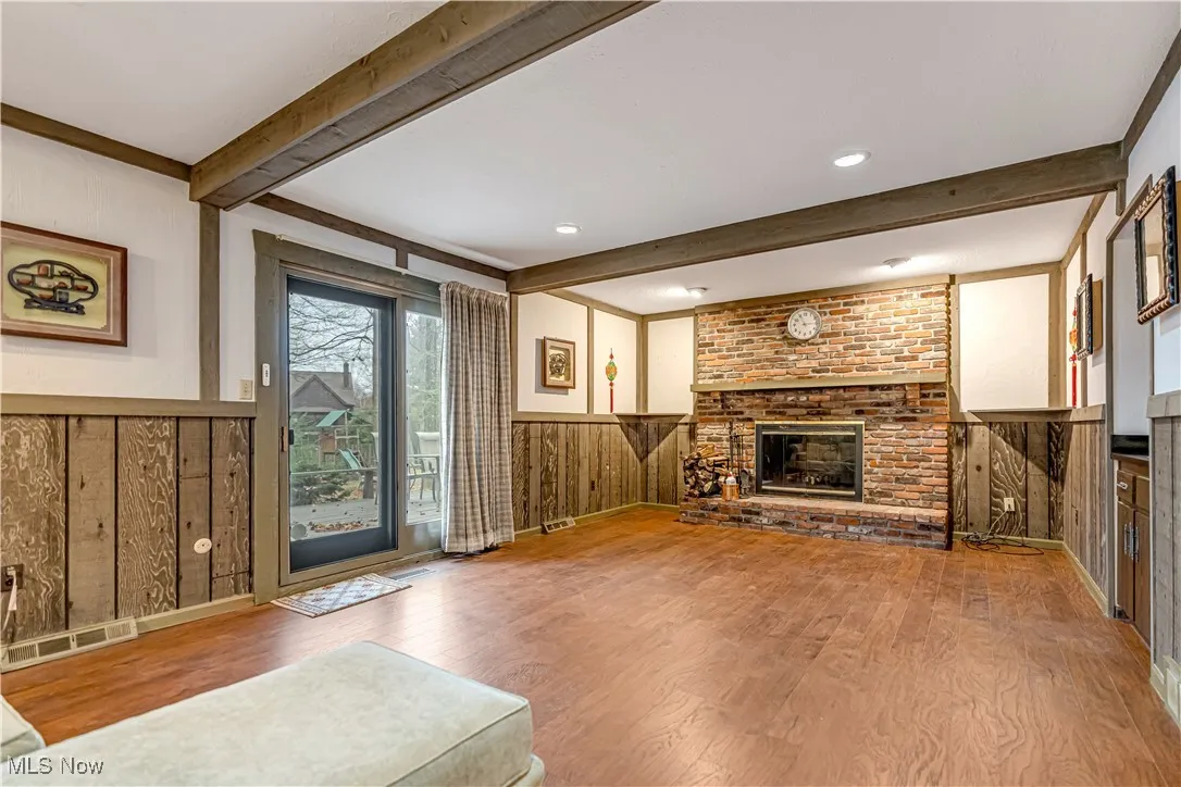 Living room with wainscoting, wood walls, wood finished floors, a fireplace, and beam ceiling