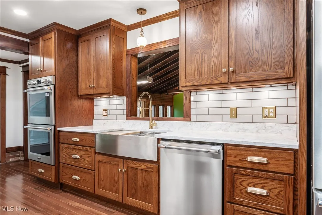Kitchen with appliances with stainless steel finishes, backsplash, light stone countertops, crown molding, and brown cabinets
