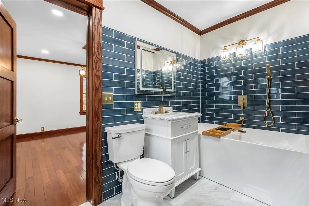 Bathroom featuring ornamental molding, vanity, tile walls, light wood-style floors, and bathtub / shower combination