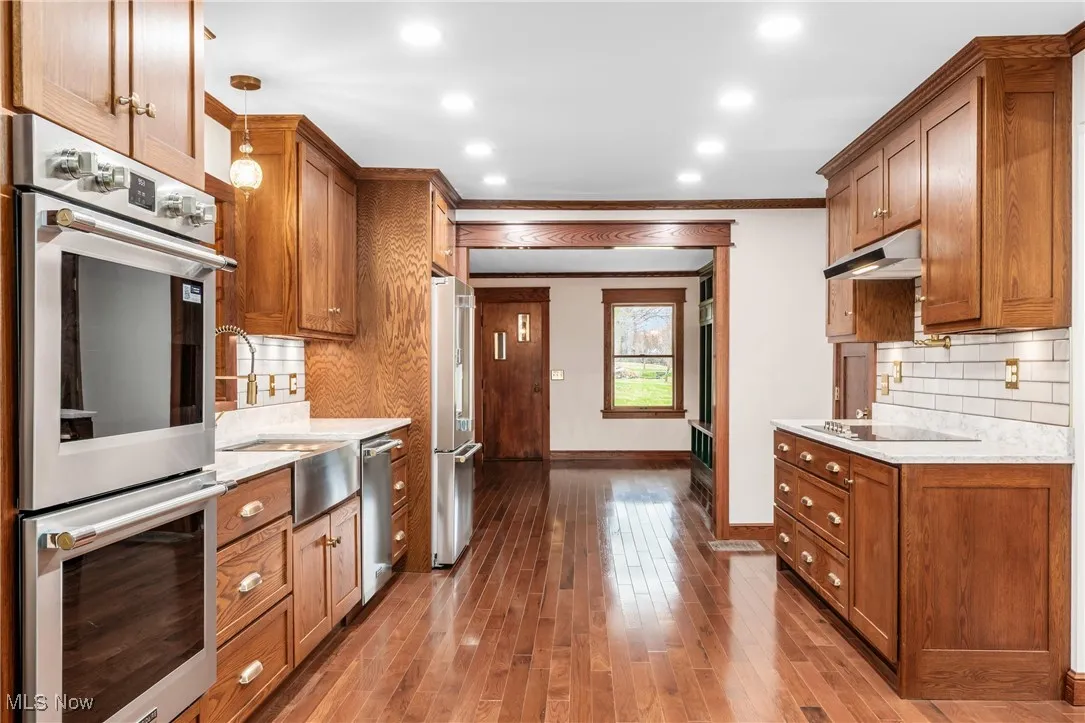 Kitchen with appliances with stainless steel finishes, brown cabinets, ornamental molding, decorative backsplash, and recessed lighting