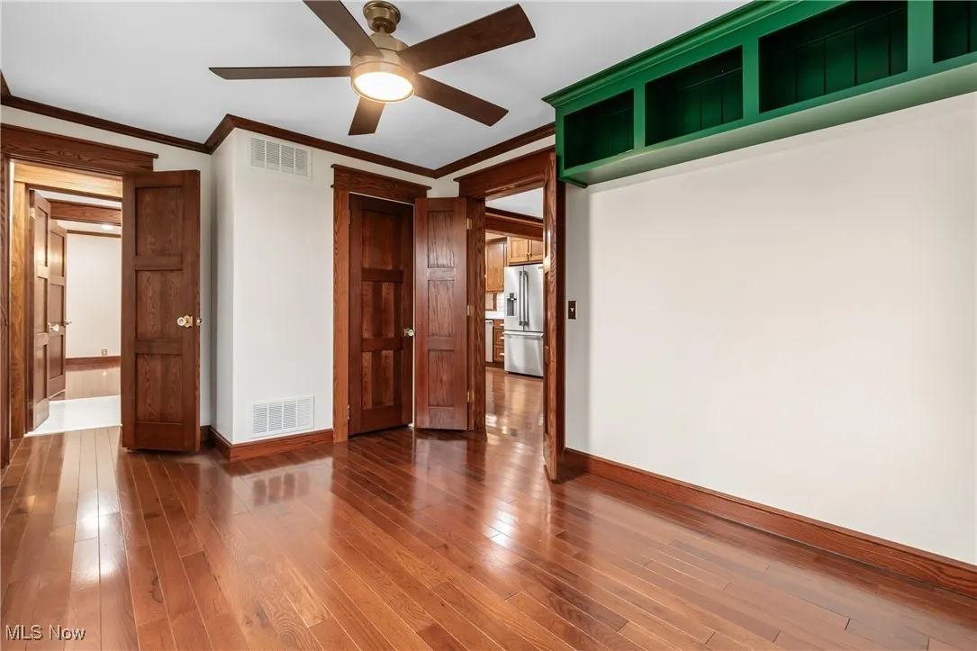 Unfurnished bedroom featuring hardwood / wood-style flooring, crown molding, high quality fridge, and ceiling fan