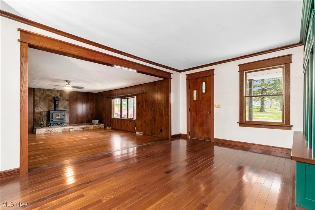 Unfurnished living room featuring a wood stove, crown molding, hardwood / wood-style flooring, wood walls, and ceiling fan