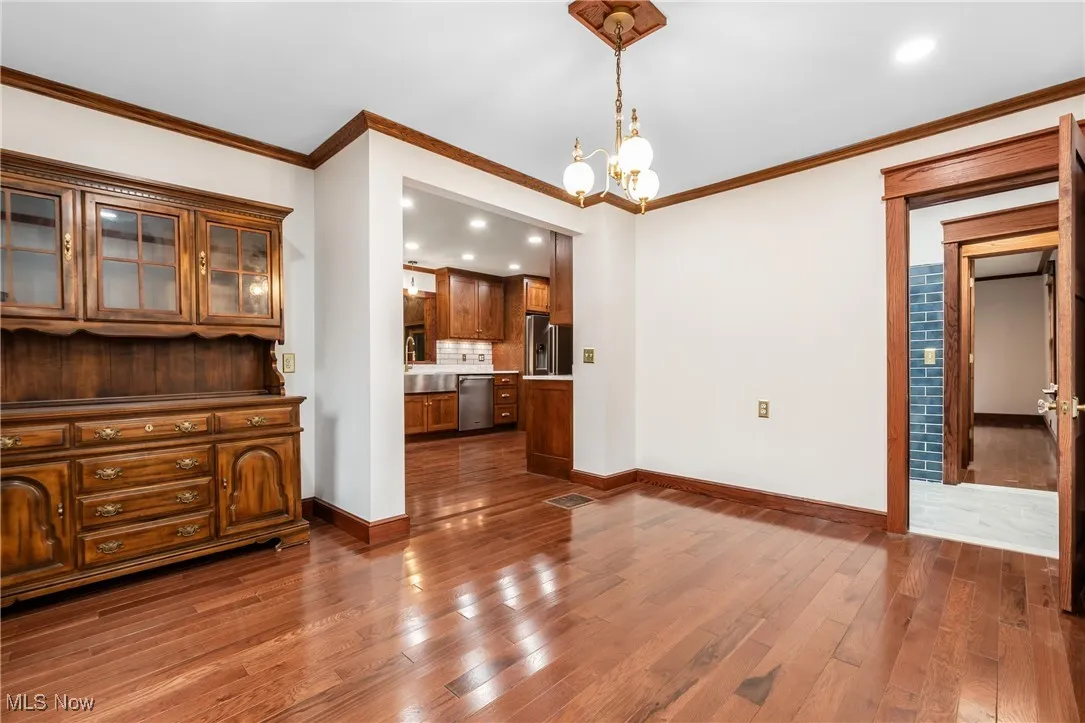 Unfurnished dining area with a chandelier, dark wood-type flooring, recessed lighting, and ornamental molding