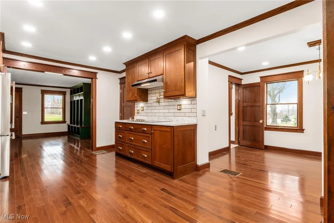 Kitchen featuring brown cabinets, crown molding, dark wood-type flooring, recessed lighting, and freestanding refrigerator