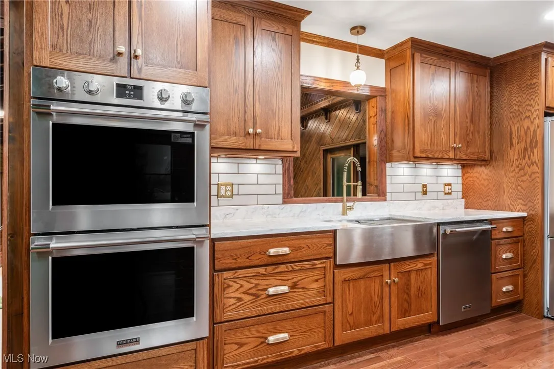 Kitchen with appliances with stainless steel finishes, backsplash, light stone counters, and brown cabinets