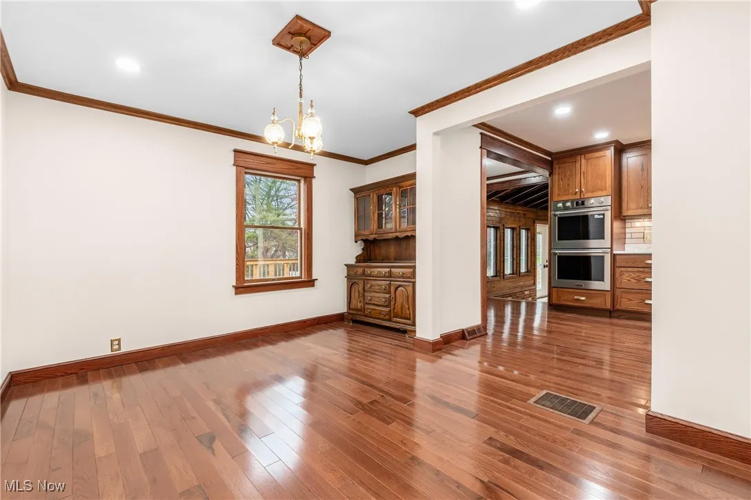 Unfurnished dining area with wood-type flooring, a chandelier, ornamental molding, and recessed lighting