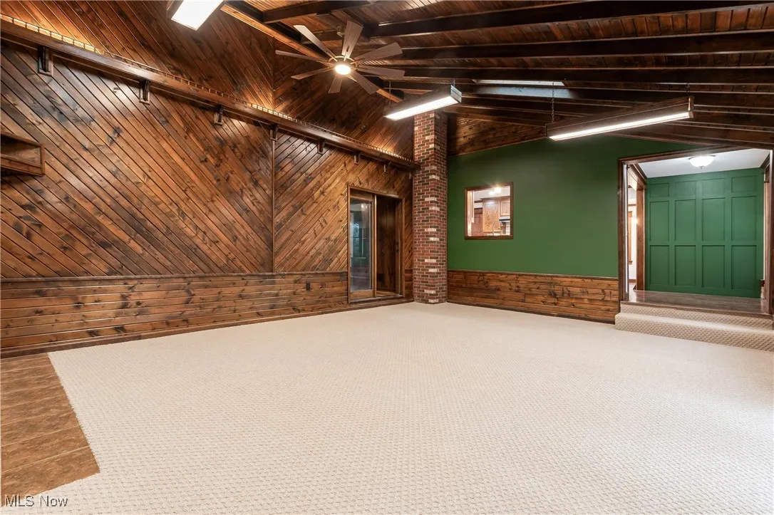 Empty room with wooden walls, a wood ceiling with exposed beams, a wainscoted wall, and high vaulted ceiling