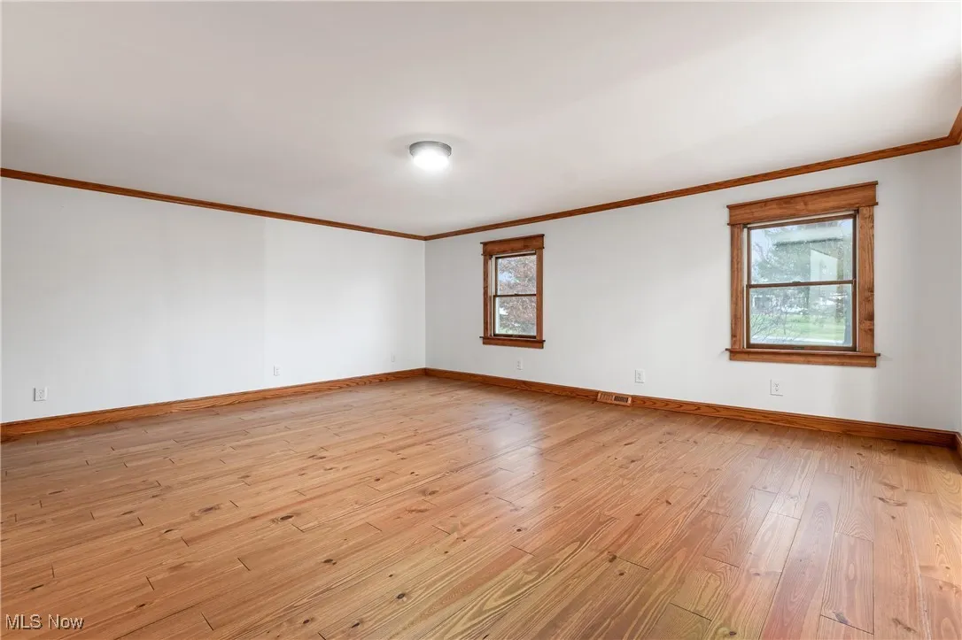 Empty room with light wood-style floors, ornamental molding, and plenty of natural light