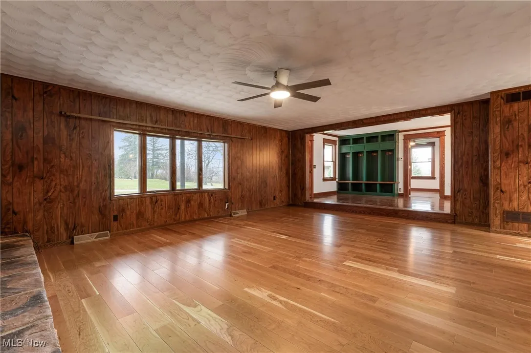 Unfurnished living room with light wood-style floors, wooden walls, ceiling fan, and plenty of natural light