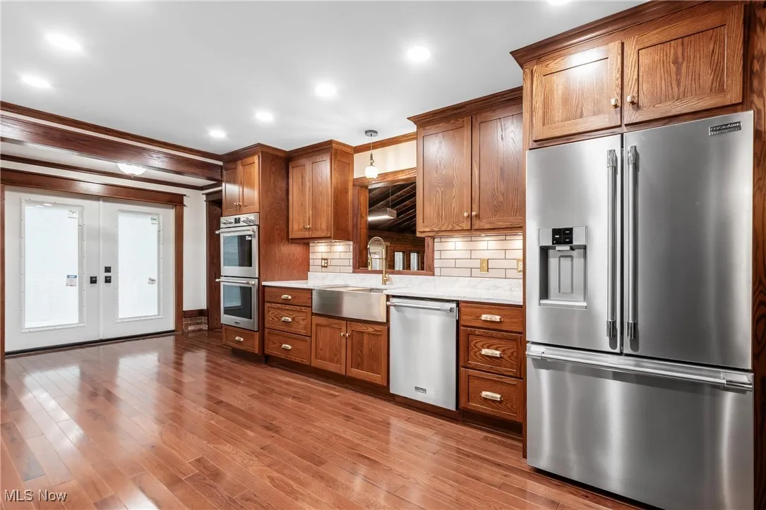 Kitchen featuring appliances with stainless steel finishes, brown cabinetry, light stone countertops, french doors, and crown molding