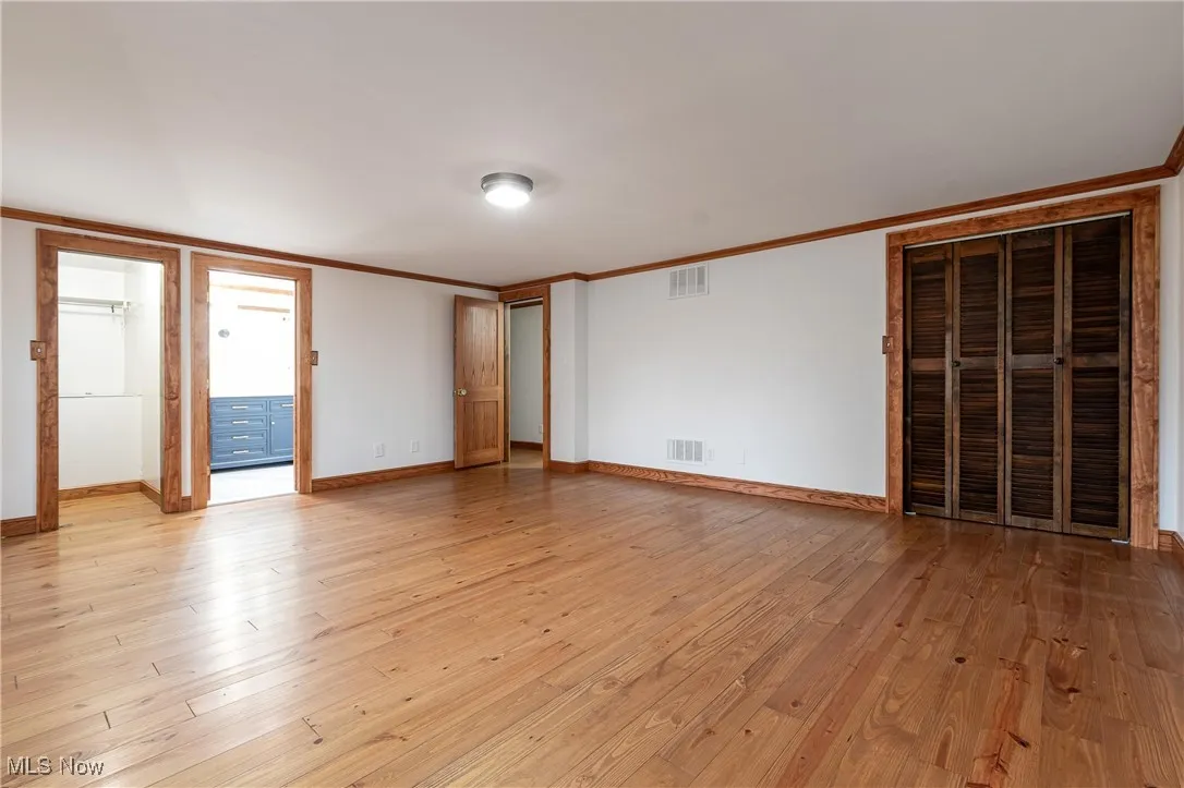 Unfurnished bedroom with light wood-type flooring, crown molding, and ensuite bath
