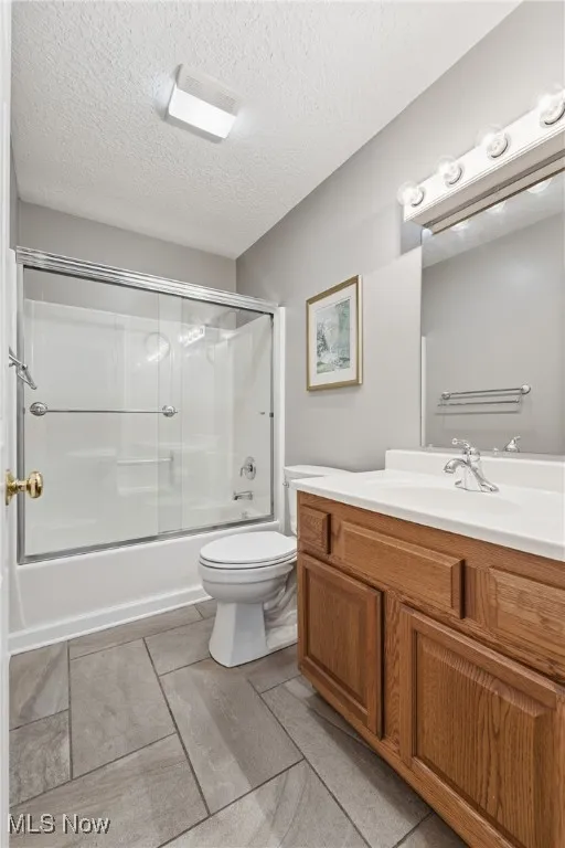 Bathroom with enclosed tub / shower combo, vanity, and a textured ceiling