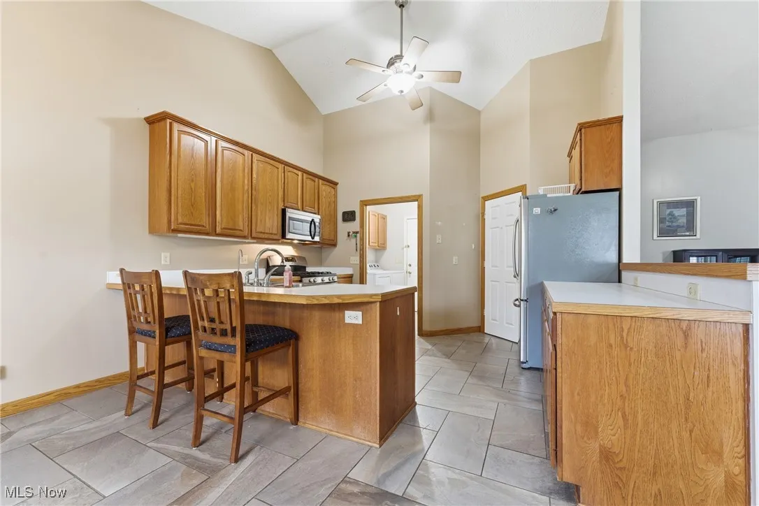 Kitchen with a peninsula, a kitchen breakfast bar, brown cabinets, light countertops, and high vaulted ceiling