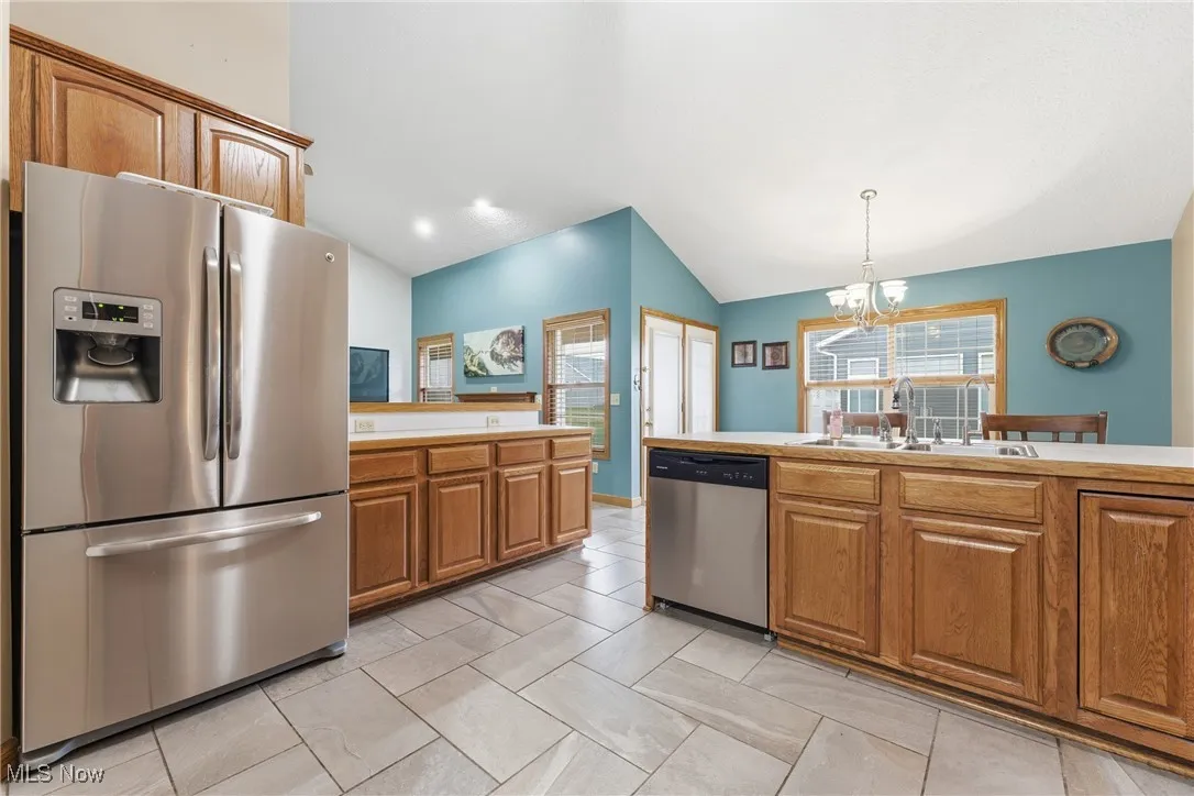 Kitchen featuring appliances with stainless steel finishes, brown cabinets, a chandelier, lofted ceiling, and light countertops