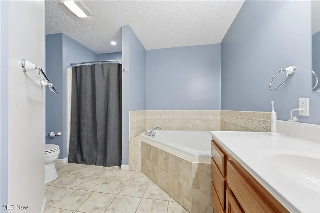 Full bathroom featuring a garden tub, vanity, a stall shower, a textured ceiling, and light tile patterned floors