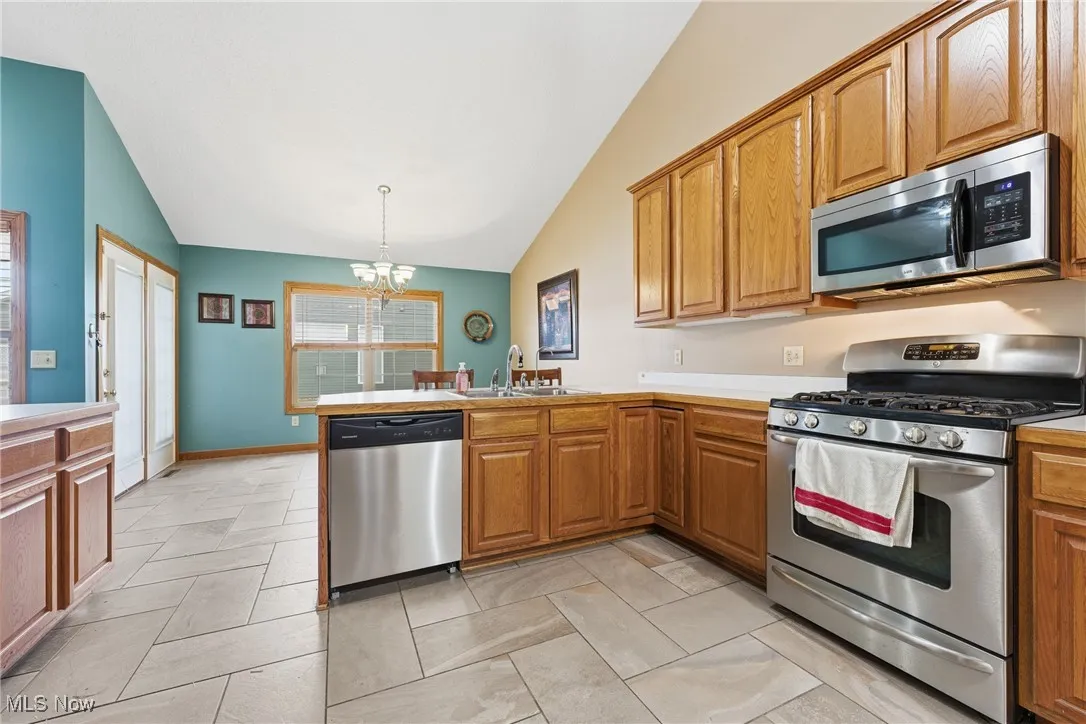 Kitchen featuring appliances with stainless steel finishes, a peninsula, a chandelier, brown cabinetry, and light countertops