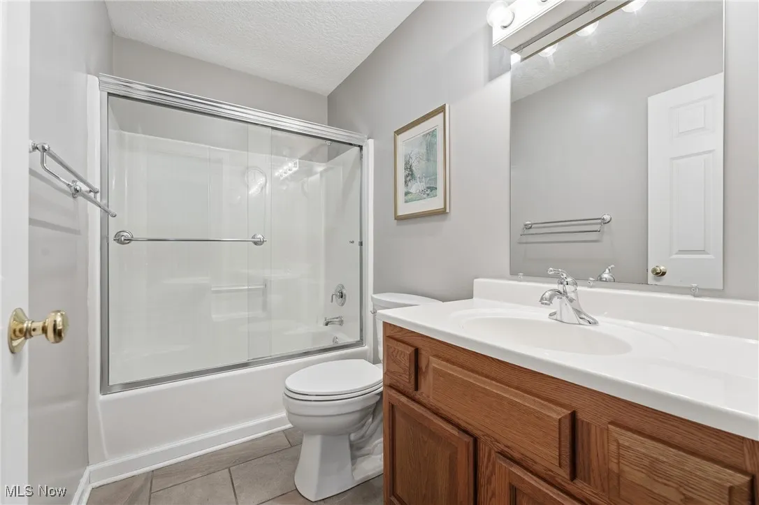 Full bathroom with a textured ceiling, bath / shower combo with glass door, vanity, and light tile patterned flooring